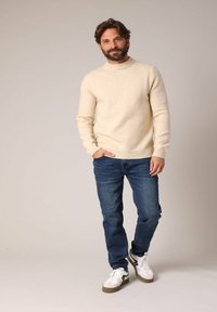 Crème-kleurige gebreide trui met een hoge hals, gecombineerd met blauwe denim jeans en witte sneakers met grijze accenten.