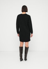 Μ αύρο πλεκτό φόρεμα με άνετη εφαρμογή, μακριά μανίκια και στρογγυλή λαιμόκοψη, συνδυασμένο με καφέ μπότες μέχρι το γόνατο.