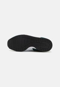 Semelle de sneaker en caoutchouc noir avec un motif de bande de roulement texturé, présentant des accents verts et une partie supérieure blanche visible sur les bords.