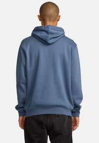 Felpa con cappuccio in morbido tessuto blu. Presenta una vestibilità comoda, polsini e orlo a costine. La vista posteriore mostra dettagli delle cuciture e un cappuccio confortevole.