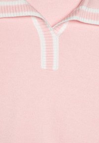 Lys rosa genser med en ribbet hvit krage og knappeåpning. Stoffet virker mykt og glatt, med en subtil, finstrikket tekstur.
