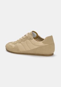 Chaussure de sport beige clair présentant un mélange de matériaux lisses et texturés, un design à lacets et un bout arrondi avec une semelle en caoutchouc plate.