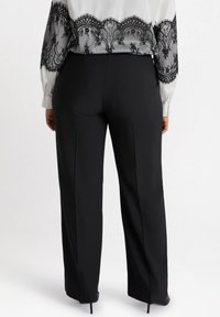 Svarta, högmidjade byxor med slät yta och skräddarsydd passform, som har rak benstil och något utsvängd nederkant.