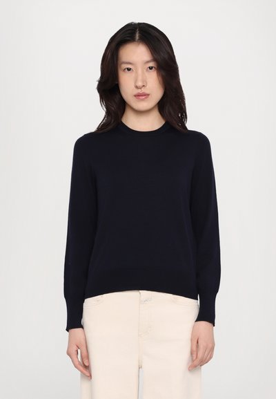 Pull à col rond côtelé en maille navy avec de longues manches, présentant une taille ajustée et une texture lisse. Assorti à un pantalon de couleur claire.