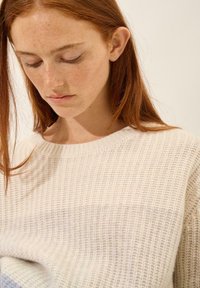 Gebreide trui in crème met een textuurpatroon. Heeft een ronde halslijn en een relaxed fit, met fijne ribbels door het geheel.