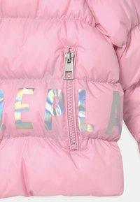 Różowa pikowana tkanina z pionowym srebrnym zamkiem błyskawicznym i odbijającymi holograficznymi literami częściowo tworzącymi słowo na tkaninie.