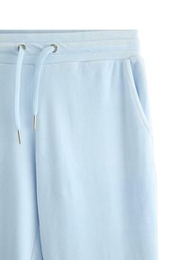 Jasnoniebieskie spodnie dresowe wykonane z miękkiej tkaniny, z elastycznym pasem i sznurkami oraz bocznymi kieszeniami. Gładka faktura i prosty design.
