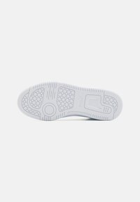 White sneaker outsole with textured rubber for grip, featuring a hexagonal pattern, circular emblem, and horizontal grooves for traction.