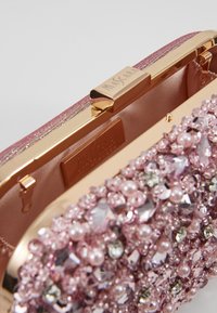 Pochette rose ornée avec un cadre en métal doré, présentant des perles et des gemmes scintillantes à l'avant, doublée d'un intérieur en satin.