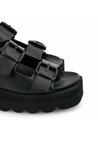 Sandalias de plataforma negras con tres correas ajustables y hebillas rectangulares. Parte superior de cuero suave, punta redondeada y suela con forma de concha.