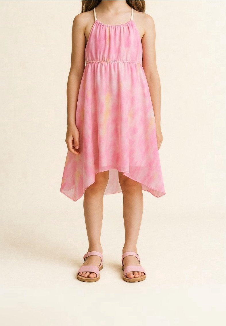 Jeune fille portant une robe rose tie and dye sans manches avec un ourlet asymétrique et des sandales roses, debout devant un fond uni.