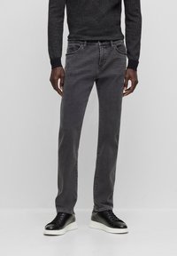 Jeans de algodón gris con corte slim, cinco bolsillos, costuras en contraste y zapatillas de cuero negras con suela blanca. Suéter texturizado negro.