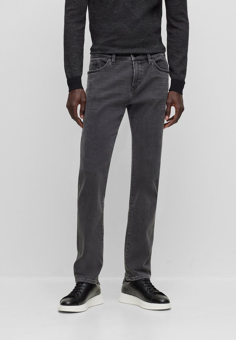 Jeans de algodón gris con corte slim, cinco bolsillos, costuras en contraste y zapatillas de cuero negras con suela blanca. Suéter texturizado negro.