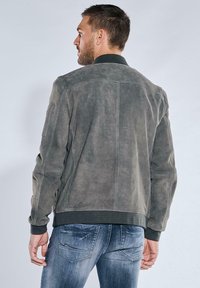 Grau Wildlederjacke mit geripptem Kragen, seitlichem Reißverschluss und taillierten Bündchen. Glatte Textur mit sauberer Naht und subtiler Gestaltung.