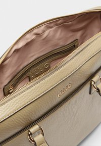 Beige leren handtas met een geribbelde afwerking, gouden hardware en een satijnen interieur. Heeft een ritssluiting en een binnenzak.