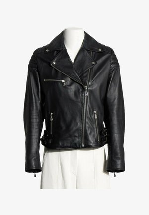 Chaqueta de motorista de cuero negro con cremallera frontal asimétrica, bolsillos con cremallera, detalles en los hombros y correas laterales con hebilla en un maniquí blanco.