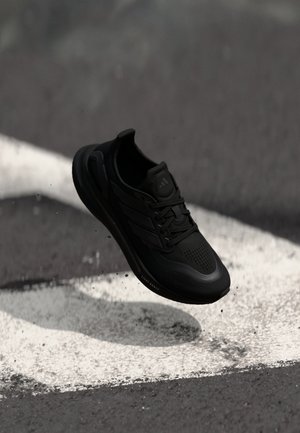 Black athletic shoe with a breathable mesh upper, textured outsole, and lace closure. Features three parallel stripes on the side.