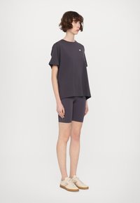 Tricou supradimensionat de culoare gri închis, cu mâneci scurte, asociat cu pantaloni scurți de ciclism asortați. Încălțămintea are un design în nuanțe de bej și maro.