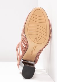 Sandale avec une semelle texturée beige, taille 37, lanières marron et talon bloc noir reposant sur une surface blanche.