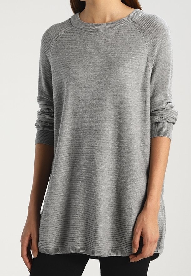 Femme portant un pull en maille côtelée gris clair à manches longues avec un col rond et un pantalon noir.