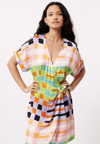 Kleurvolle wikkeljurk met een geruit patroon in roze, groen, oranje en zwart. Gemaakt van lichtgewicht stof met korte mouwen.