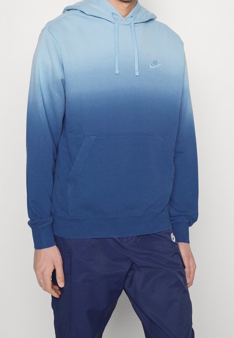 Sudadera con degradado azul hecha de una mezcla de algodón, con un bolsillo canguro y capucha con cordón. Logo de Nike bordado en el pecho.