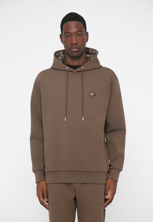 Haut à capuche marron en matériau doux, doté d'une poche avant, d'une capuche à cordon de serrage et d'un intérieur à motifs. Accents en métal argenté.