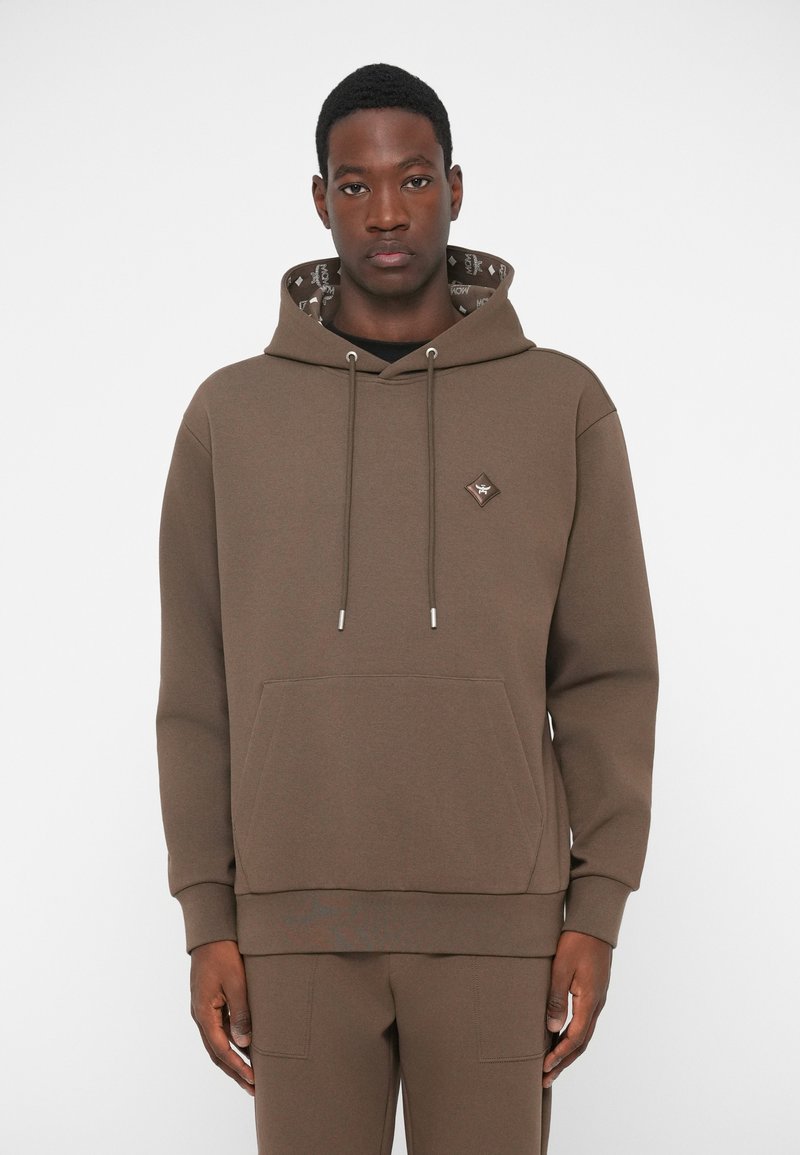 Brązowa bluza z kapturem wykonana z miękkiego materiału, z przednią kieszenią, kapturem ze sznurkiem i wzorzystym wnętrzem. Akcenty w kolorze srebra.