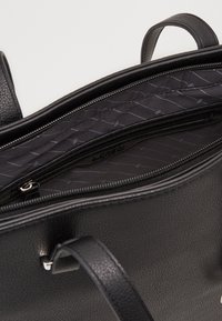 Schwarze Lederhandtasche mit strukturierter Oberfläche, mit Reißverschluss versehenen Fächern und einem glatten, dunklen Stofffutter mit einem dezenten Muster.