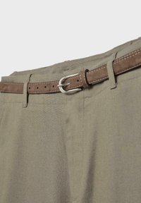 Gros plan d'un pantalon kaki avec une ceinture en daim marron passée dans les passants de ceinture et une boucle en métal argenté attachée.