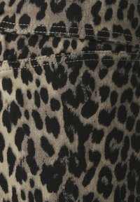 Tissu imprimé léopard en noir et beige, avec une texture douce et des taches irrégulières, et des détails de couture visibles.