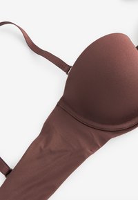Soutien-gorge rembourré marron avec bretelles réglables sur fond blanc, montrant un tissu lisse et des détails de couture.