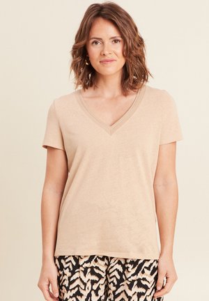 Beige Kurzarm-V-Ausschnitt-T-Shirt mit strukturiertem Ausschnitt, getragen mit gemusterten schwarzen und cremefarbenen Hosen. Weicher Stoff, lockere Passform.