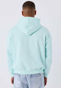Sweat à capuche bleu clair en tissu doux, doté d'une capuche avec cordon de serrage et de poignets côtelés ; la vue de dos montre des coutures minimales et aucun détail supplémentaire.