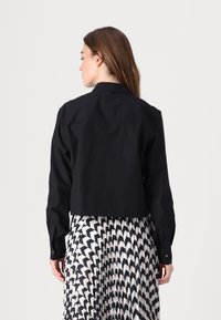 Cropped shirt nera in cotone con maniche lunghe, colletto a punta e polsini con bottoni, abbinata a una gonna pieghettata bianca e nera.