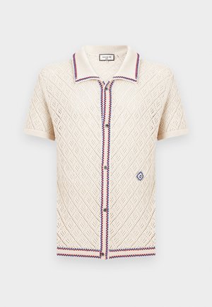 Cardigan en maille crème à manches courtes avec ajourés en forme de losange, bordures rouges et bleues au niveau du col, de la patte de boutonnage et de l'ourlet, et un petit logo brodé.