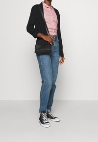 Svart kavaj över en rosa skjorta med krage, tillsammans med ljusblå högmidjade jeans och svarta högskaftade sneakers. Enkel svart axelremsväska.