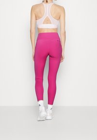 Różowe legginsy z wysokim stanem i gładką teksturą, połączone z jasnoróżowym stanikem sportowym z tylnym zapięciem w stylu racerback i wycięciem.