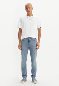 Hvit t-skjorte med korte ermer, lyseblå rette jeans og blå joggesko. Antrekket har et enkelt design og en avslappet passform.