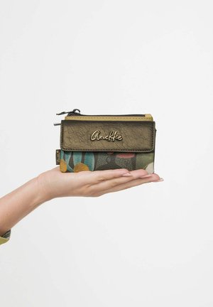 Hand hält eine kleine braune und mehrfarbige Geldbörse mit Anekke-Logo und Reißverschluss vor weißem Hintergrund.