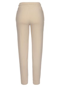Beige Jogginghosen aus weichem Stoff, mit einem elastischen Bund, Seiten Taschen und elastischen Bündchen an den Knöcheln.