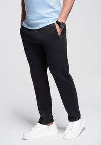 Zwarte joggingbroek met een slim fit, zijzakken en een comfortabele stof, gecombineerd met witte sneakers en een lichtblauwe shirt.
