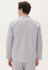 Camisa de botones a rayas en tejido ligero, con rayas verticales blancas y azul marino, mangas largas y un cuello plano en la parte posterior.