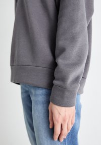 Grå bomullsgenser med ribbestrikkede mansjetter, med en avslappet passform og jevn tekstur, sammen med lyseblå denimjeans.