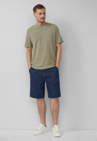 Olijfgroene t-shirt met korte mouwen gecombineerd met blauwe denim shorts en witte sneakers. De outfit heeft een casual ontwerp met een comfortabele pasvorm.