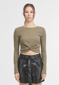 Olivově zelený vroubkovaný crop top s dlouhým rukávem a detailním kroucením vpředu, v kombinaci s černou sukní z umělé kůže s vysokým pasem a detailem na zavázání.