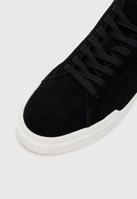 Tenis negri din suede cu o parte superioară texturată, dotat cu o talpă din cauciuc albă, șireturi negre și detalii subtile de cusături. Design cu vârful rotunjit.