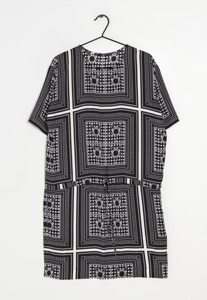 Vestido corto de manga corta en blanco y negro con patrones geométricos y florales en forma de cuadrado, colgado en una percha negra sobre un fondo blanco.