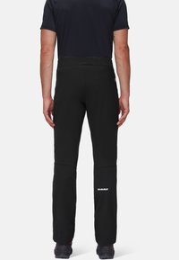 Pantalons softshell noirs avec une coupe ajustée, poches zippées et logo sur la jambe inférieure. Caractéristiques d'une texture lisse et d'une taille élastique.