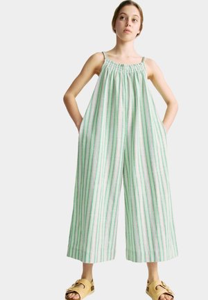 Jumpsuit a rayas verdes y blancas con diseño de pierna ancha, escote elástico y bolsillos laterales. La modelo lleva sandalias marrones.